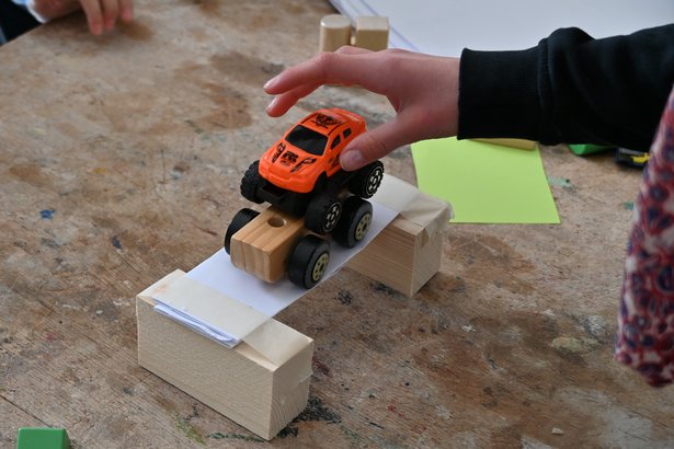 kleines Brückenbau Experiment mit zwei Holzklötzen, ein Stück Pappe und einem handgroßen Traktor