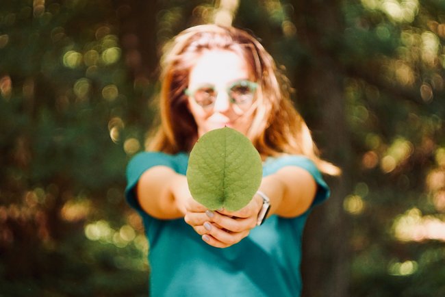 Eine Teenagerin mit Sonnenbrille hält ein großes, grünes Blatt in die Kamera.